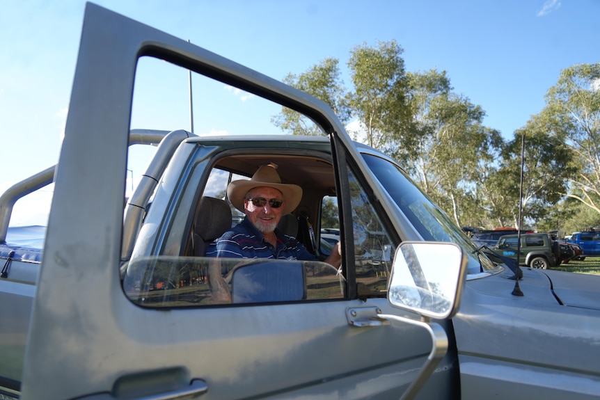 Man sits in car smiling with door open and window down 