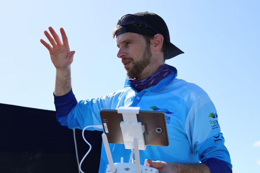 A man with a backwards black cap holds an electronic device while explaining how to spot dugongs.