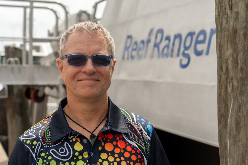 Portrait of a man on a boat in a mangrove creek wearing glasses with photochromic lenses and an indigenous-designed shirt.
