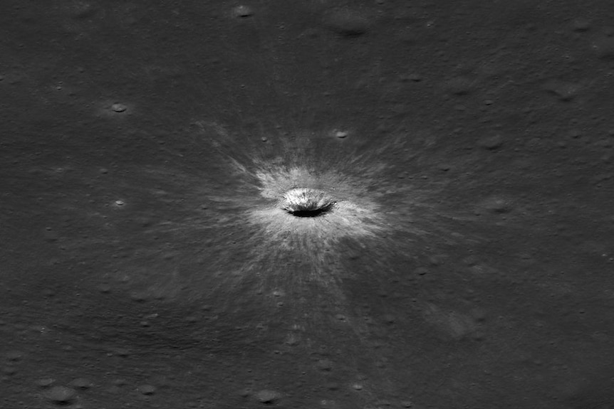 A greyscale image of a large Moon crater seen from the side, surrounded by a lighter patch of surface impact area.