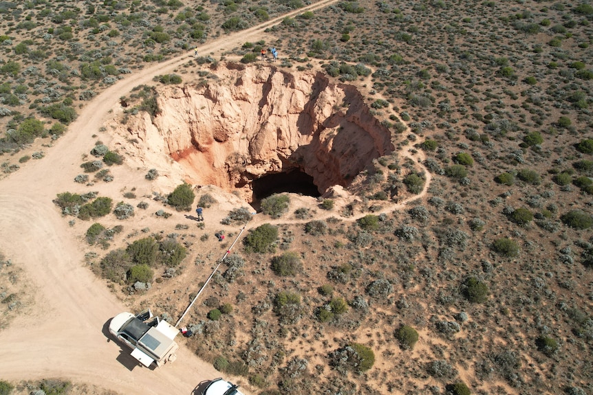 A drone shot of shrub land with a cave opening in the middle