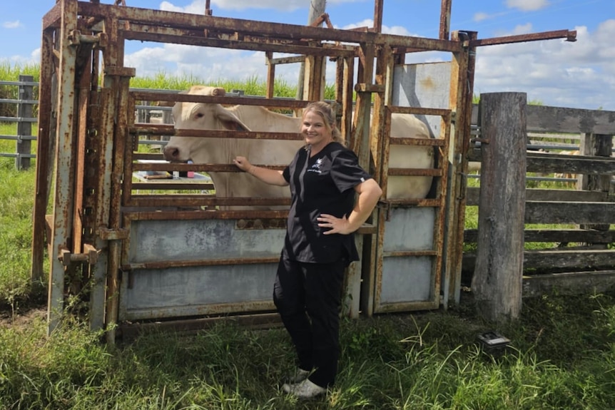 A woman leans slightly against the gate while a cow stands besides her.