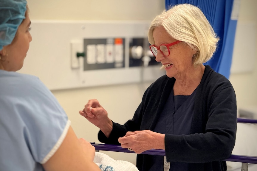 A woman with a blonde bob and red spectacles laughs with a patient.