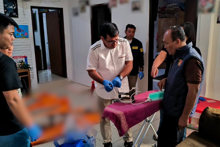 A group of police and a medical examiner work inside a room in Bali.