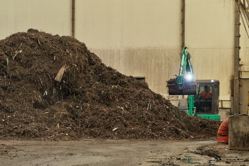 A green bulldozer at work next to a pile of brown waste.
