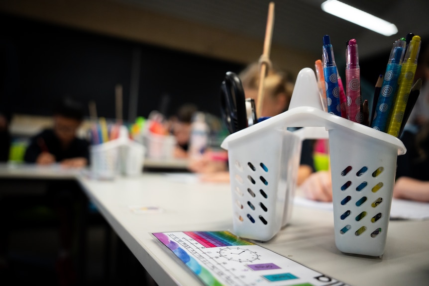 A tin of pencils and crayons on a school desk.