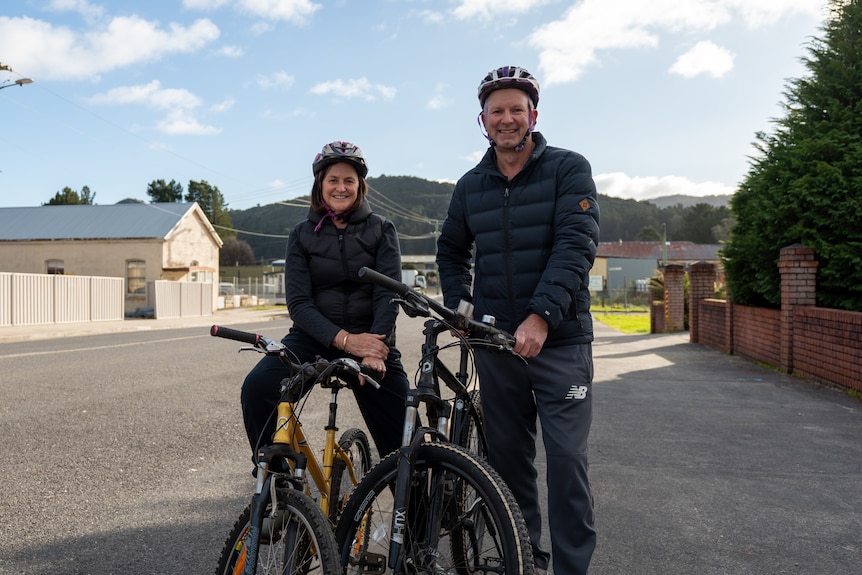 Man and woman wearing helmets, stand with their bikes on a street