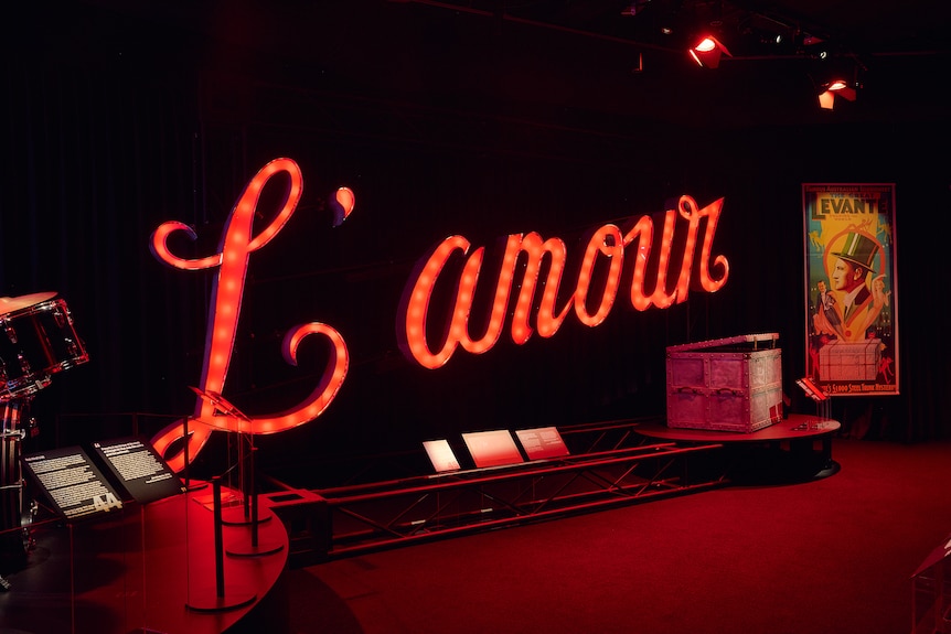A red neon sign says "L'amour" in cursive writing and sits with other props.
