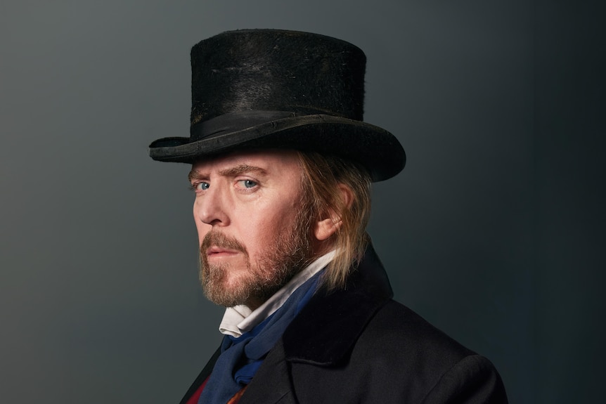Tim Minchin, 50, dressed in a top hat and old-fashioned suit, side-eyes the camera.