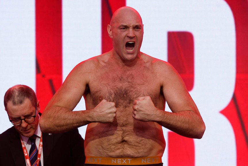 Tyson Fury with no shirt on jeering while flexing his arms with his two fists directed at one another.
