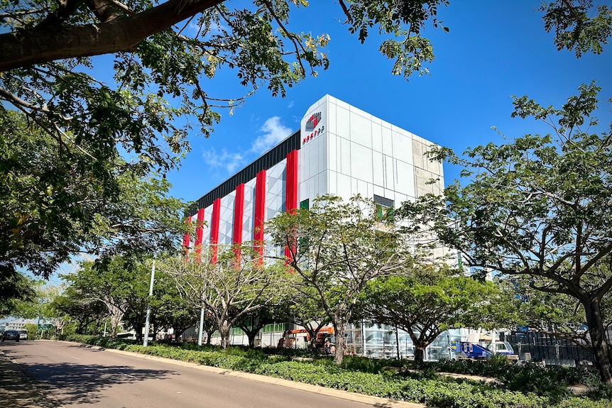A large building with grey and red cladding on a tree-lined street.