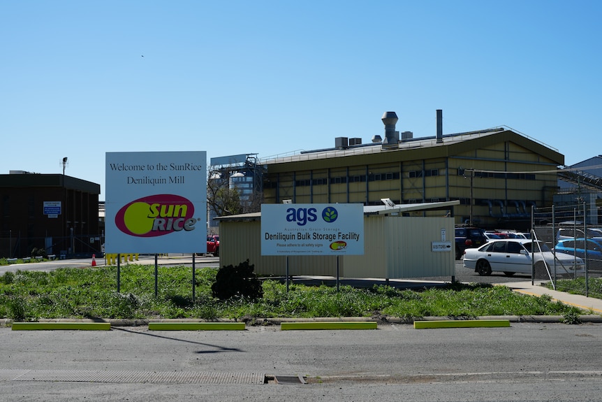 A series of industrial sheds with signs in front saying "SunRice" on one and "ags Deniliquin Bulk Storage Facility" on another.
