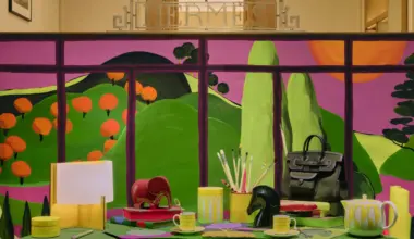 Colourful Hermès window display featuring Sarah Martinon's illustrated garden scene with vibrant pink, green and orange tones, styled with handbags, accessories and homeware products