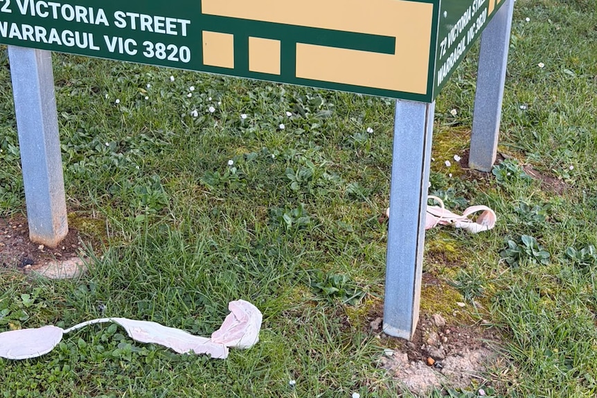 Two rashers of bacon lie on the grass underneath a sign.