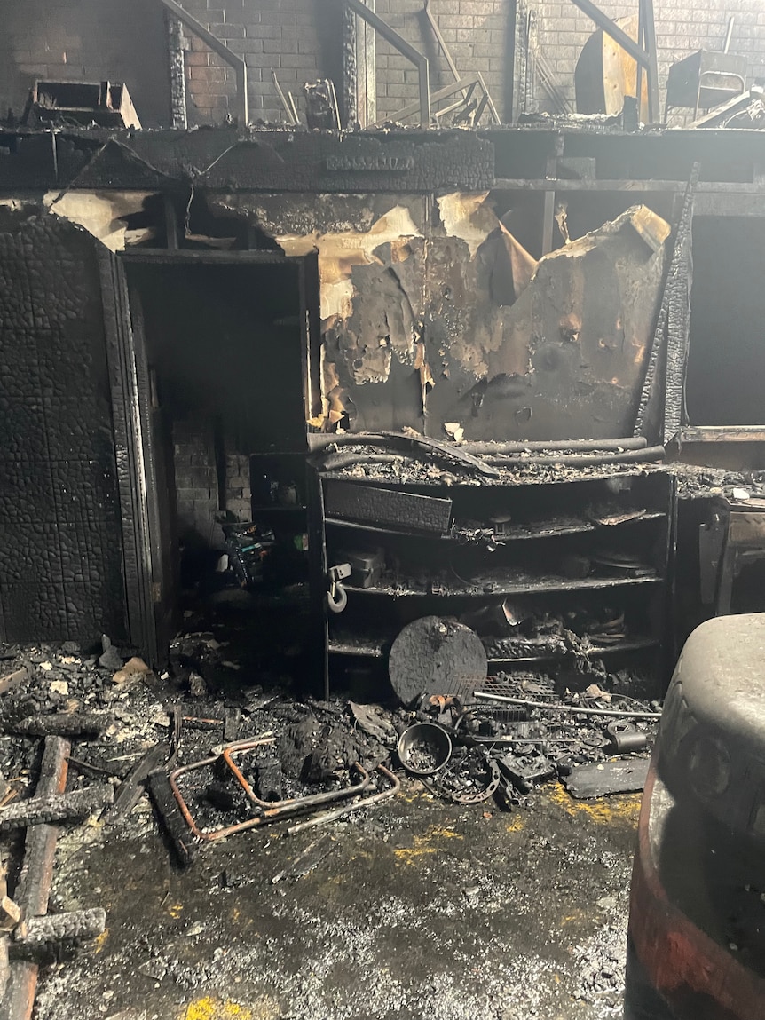A fire-blackened warehouse space, including shelves and workshop equipment covered in ash.