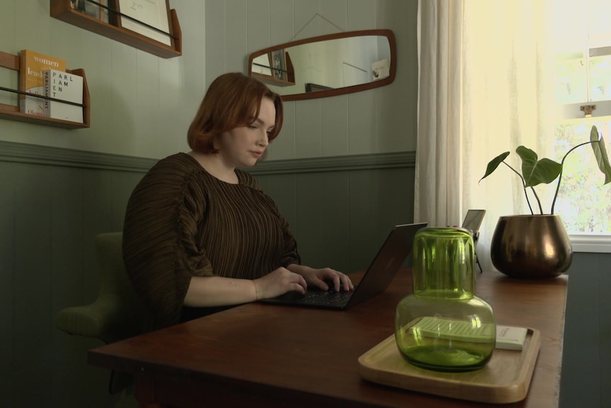 Elly Desmarchelier site at a table in a dark room looking at computer.