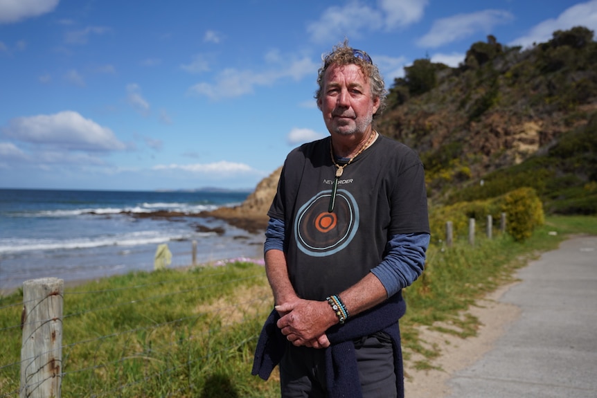A man stands on a path near a beach and cliffs.