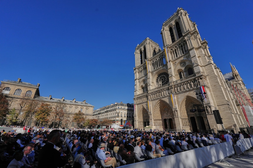 Thousands of people sit on chairs outside in front of a church.