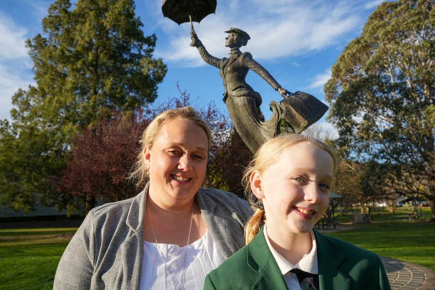 A woman and daughter sit in front of a statue of Mary Poppins.