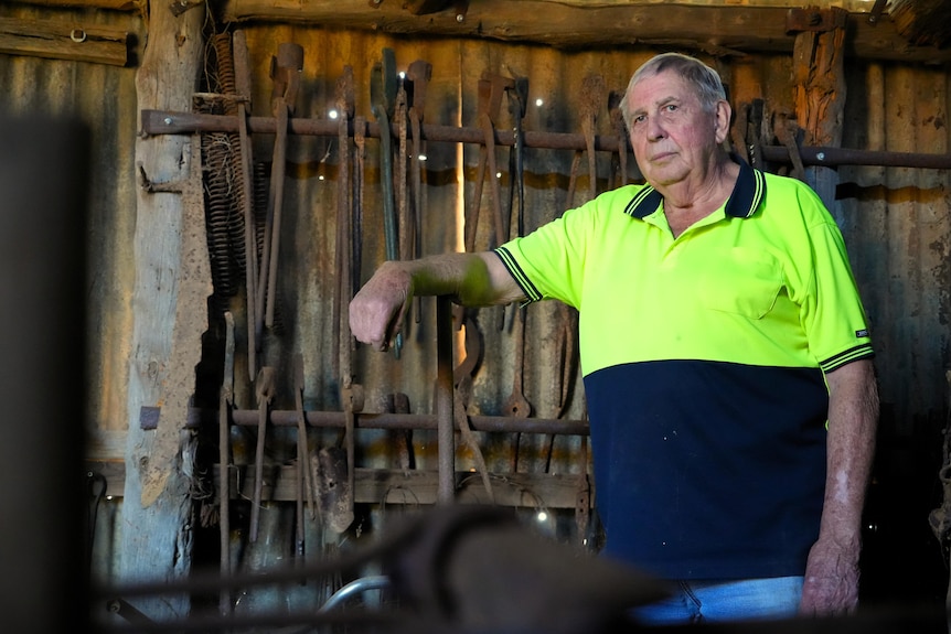 man stands in shed looking out leaning on shovel
