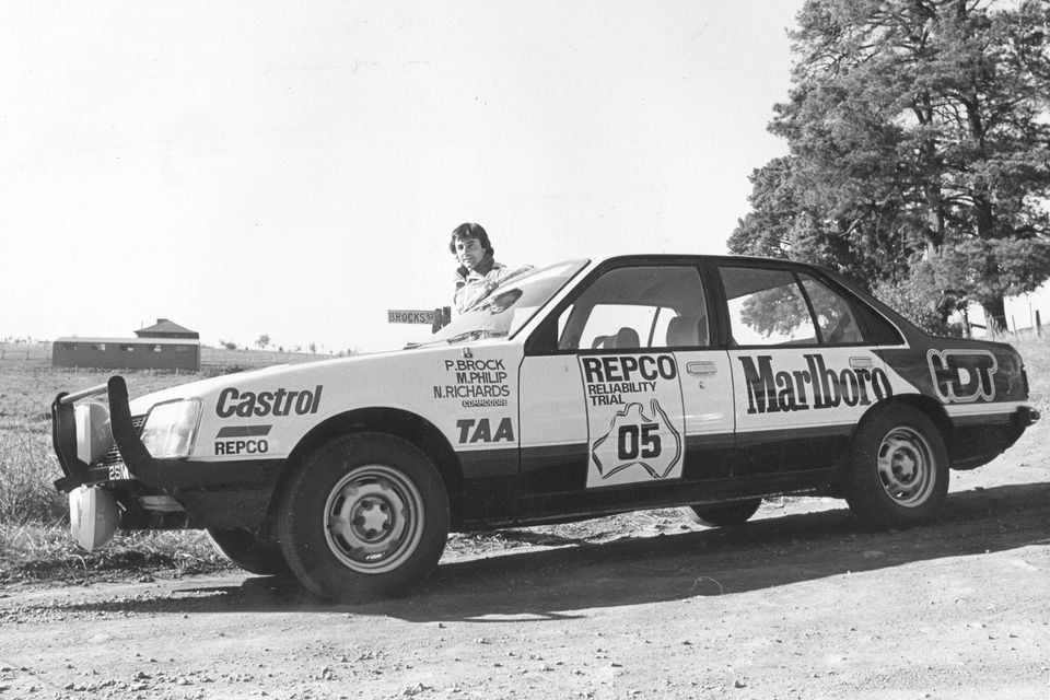 Peter Brock leaning out of a Holden VB Commodore sedan bearing Castrol, Marlboro, Repco and HDT livery, competing in the 1979 Repco Reliability Trial on a dirt road in rural Australia