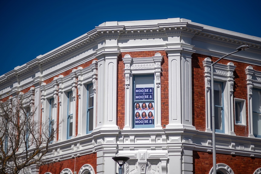 A red building with white frames under a blue sky with photos of a smiling football player in the window.