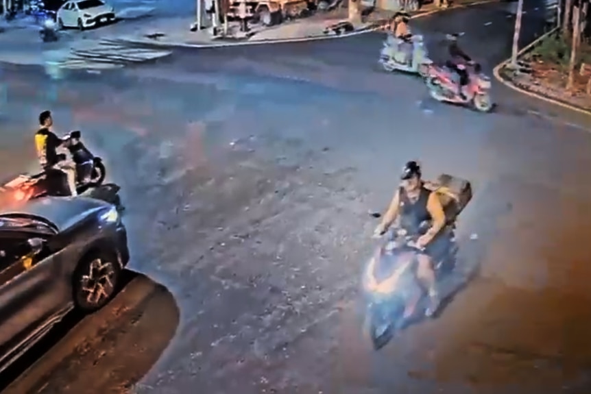 CCTV vision of a road, showing a man riding a motorcycle with a suitcase on the back.