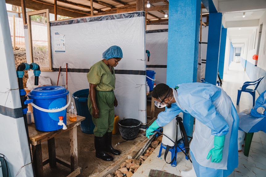 a woman in scrubs is sprayed down by a person in protective gear 