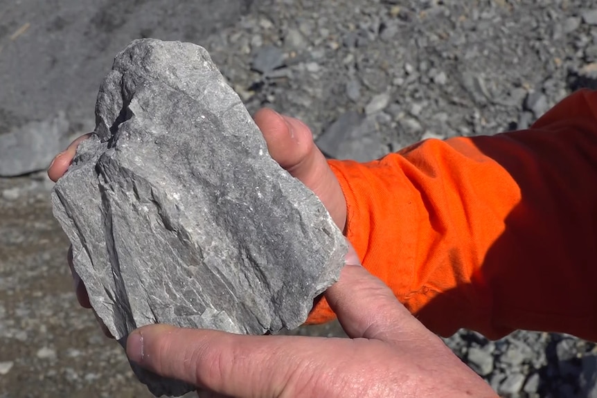 Hands hold a grey rock with little shiny specks within it