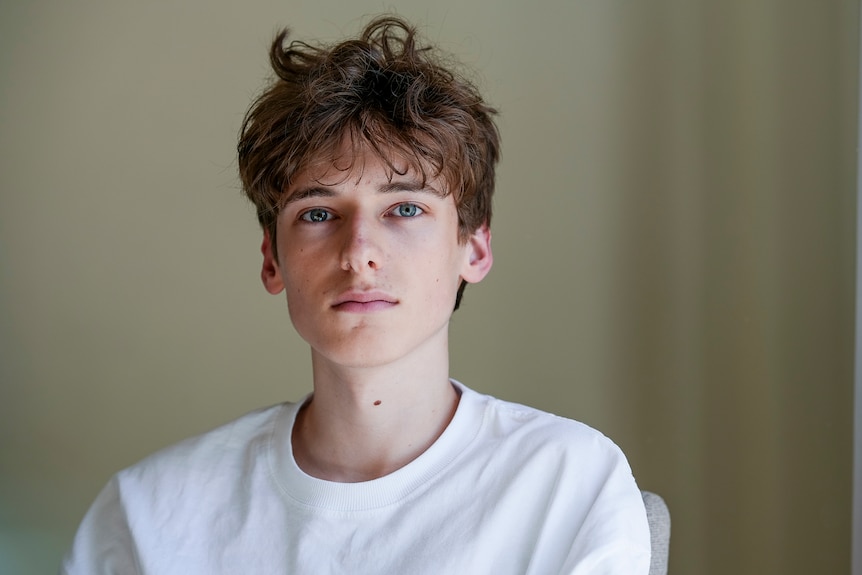 A young man with curly brown hair wearing a white tshirt