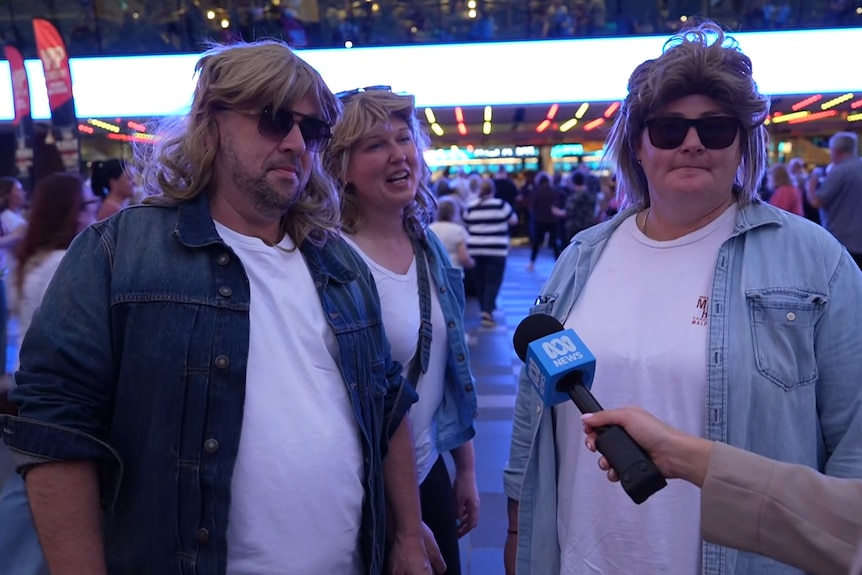 Three people with John Farnham-style wigs.