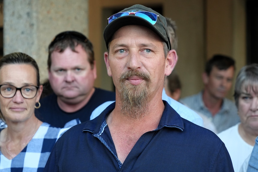A young man wearing a blue shirt with a goatee and cap. 