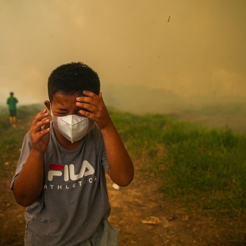 A boy in a mask runs with smoke in the background.