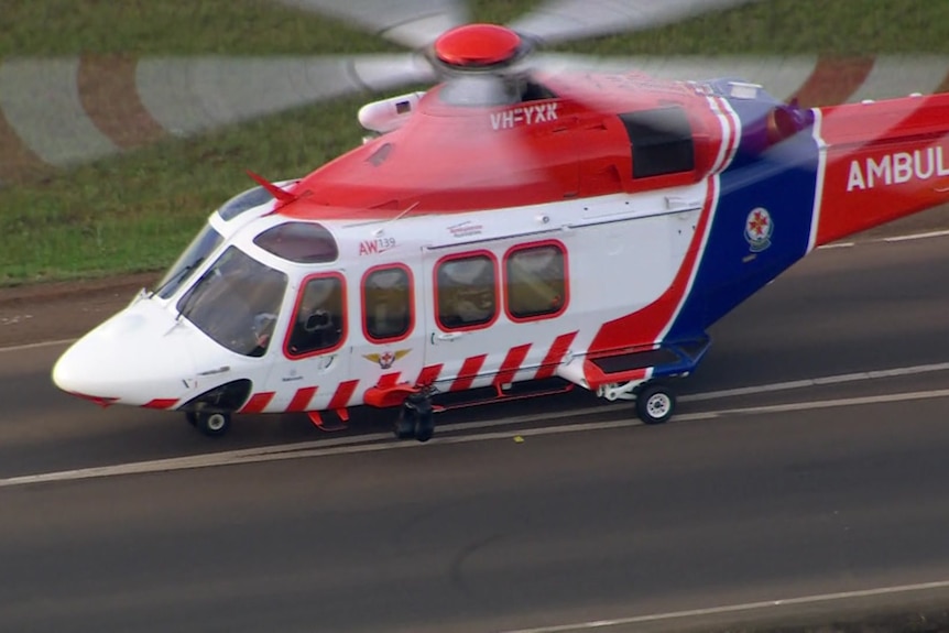 A mostly red and white helicopter with a blue strip and the word "ambulance" sits on a roadway.