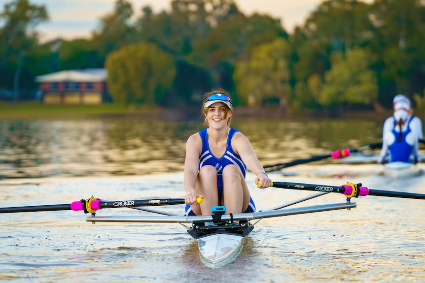 A young female rower smiling as she rows on a river.