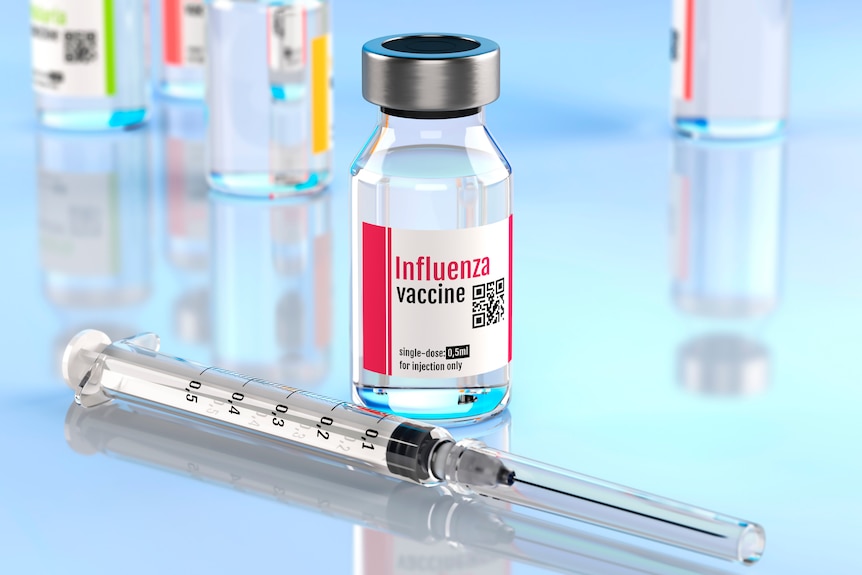Close up of a influenza vaccine vial and needle with other vials in background.