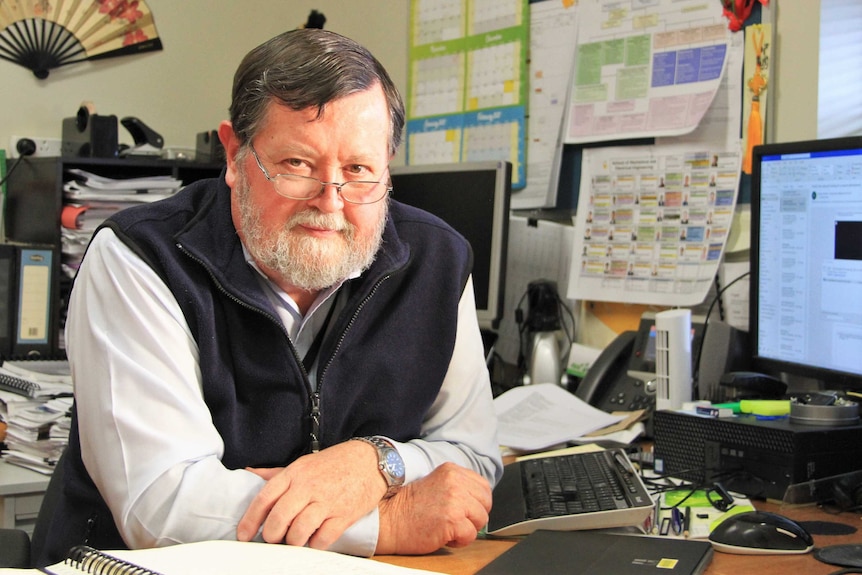 An academic sits at a desk in his office.