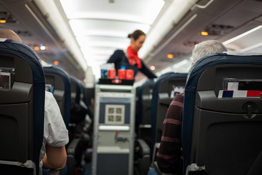A flight attendant pushing a cart on a plane.