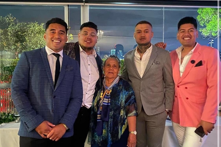 A family photo of four young men and an older woman smiling