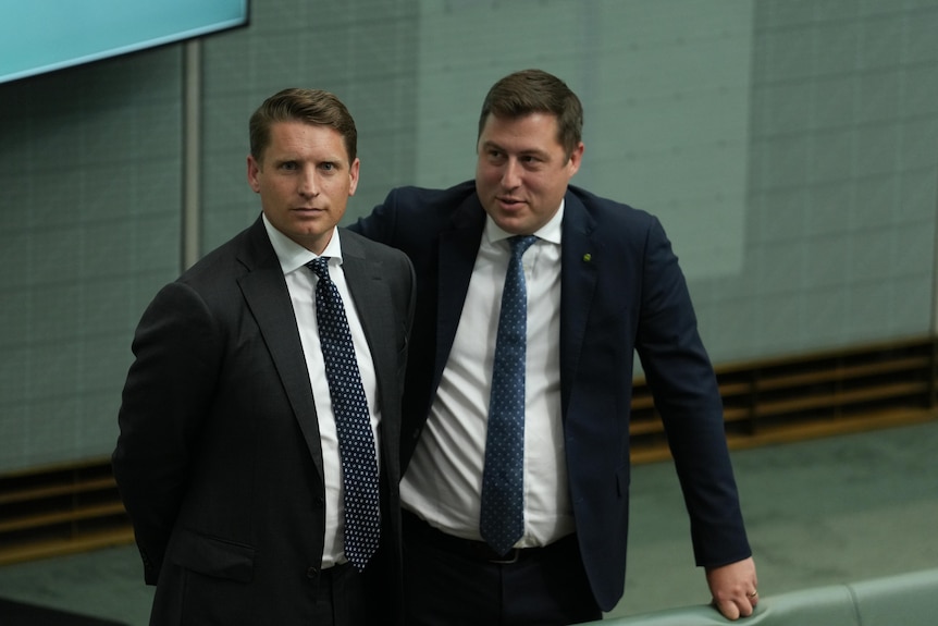 two male politicians wearing suits standing close to each other in the chamber