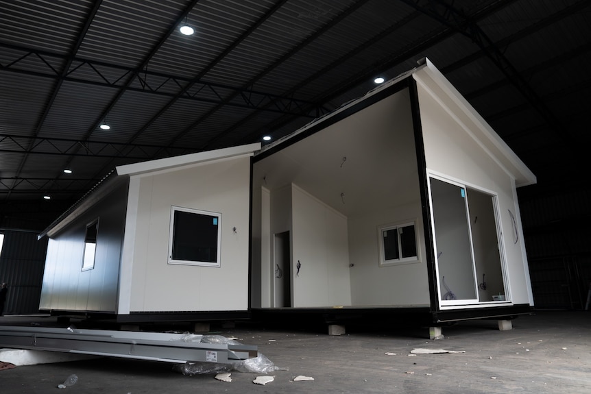 a partially finished home with white walls is pictured in a massive warehouse