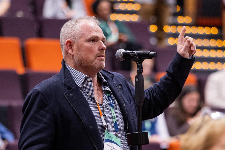 A man standing at a microphone asking a question with his hand raised