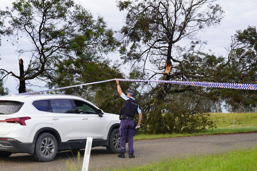 Police officer holds up tape to let car pass through