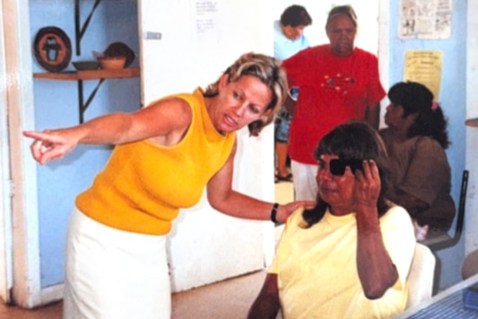 A young blonde woman points to the left to show an Aboriginal lady with an eye patch where to look.