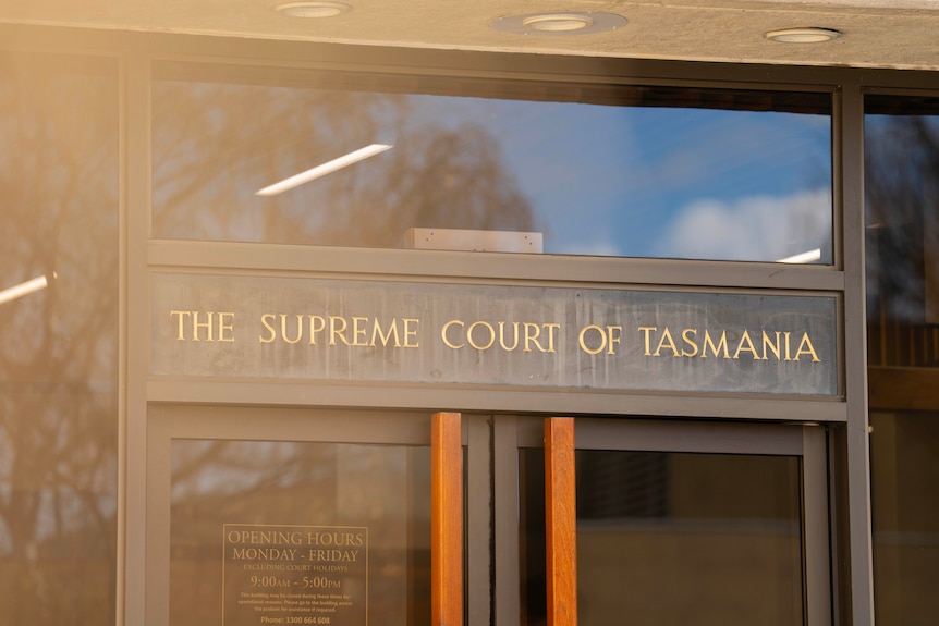 A sign at the front of a glass and brick building which reads 'Supreme Court'.