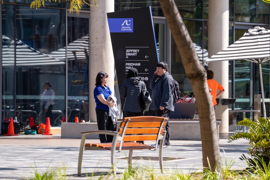 three students talk in front of the new Adelaide University sign