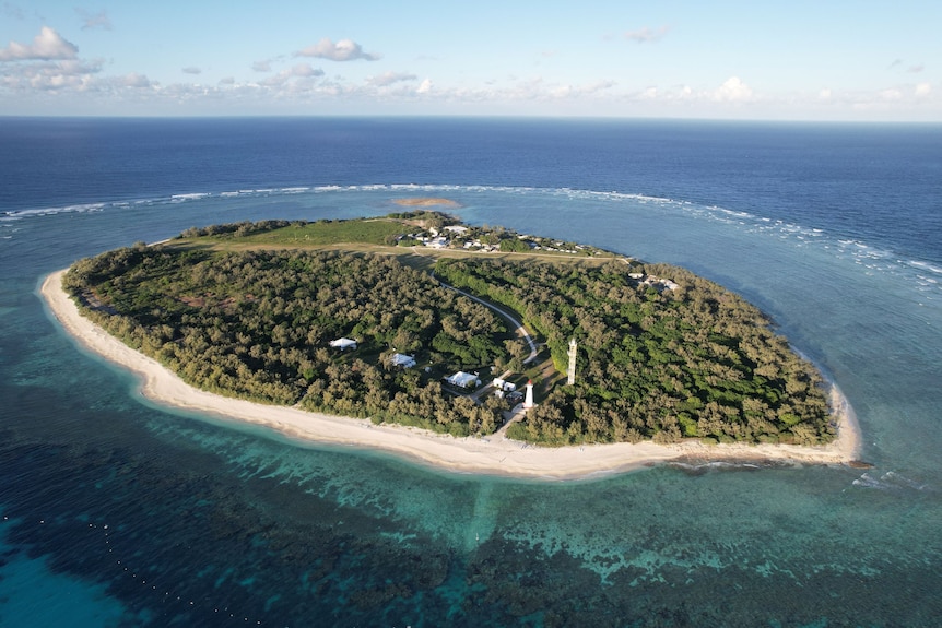 A drone image of a small island surrounded by coral beds in the middle fo the ocean.