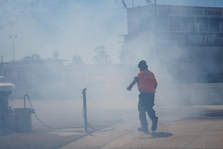 A race car official is covered in smoke following a burnout 