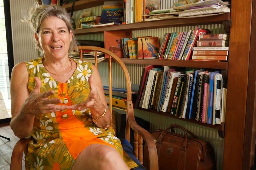 A woman sitting in a chair with a large bookcase behind her