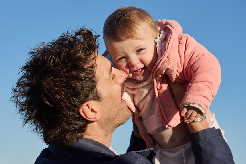 Matthew Johnson lifts up his smiling baby.